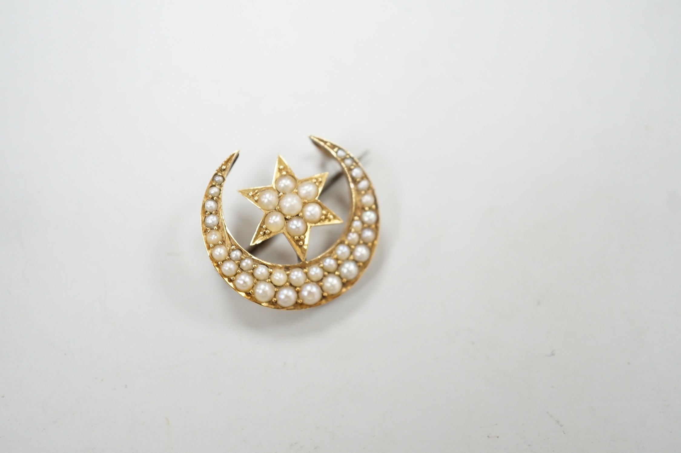 An Edwardian yellow metal and seed pearl set crescent moon and star brooch, 22mm, gross weight 4 grams.